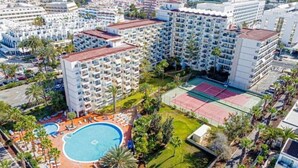 Ein Hochhaus-Hotel mit mehreren Balkonen, einem Swimmingpool und Tennisplätzen.