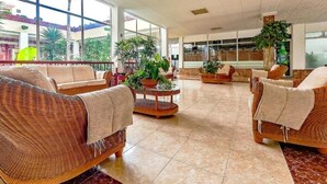 Eine geräumige Lobby mit Rattanmöbeln, großen Fenstern und Topfpflanzen.