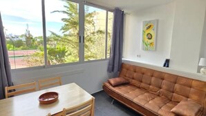 Ein Zimmer mit einer Couch, einem Esstisch und Stühlen. Ein Fenster bietet Blick auf Grünflächen und Gebäude.