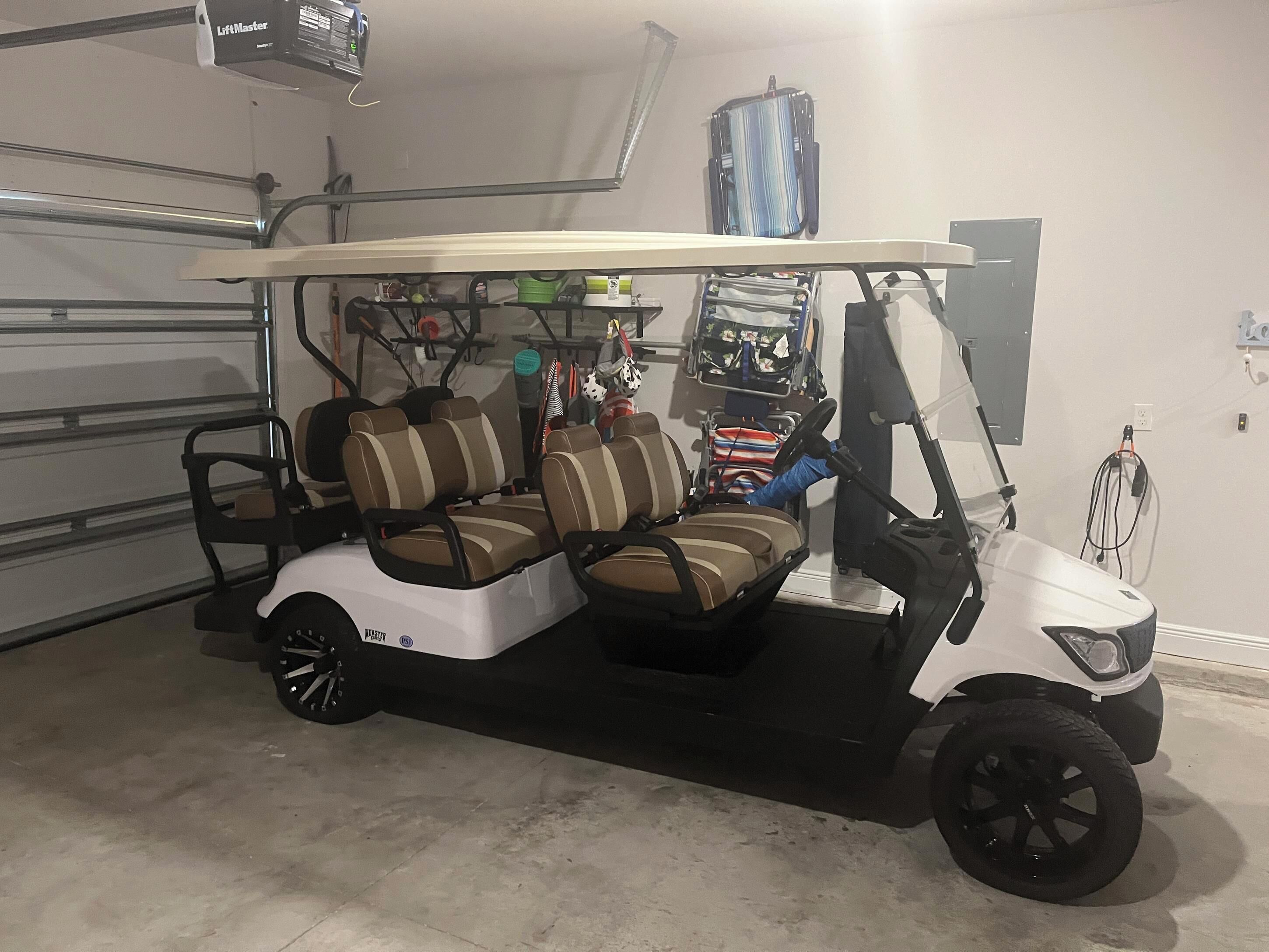 Un carrito de golf con carrocería blanca y asientos marrones, estacionado en un garaje con piso de concreto y una lámpara en el techo.