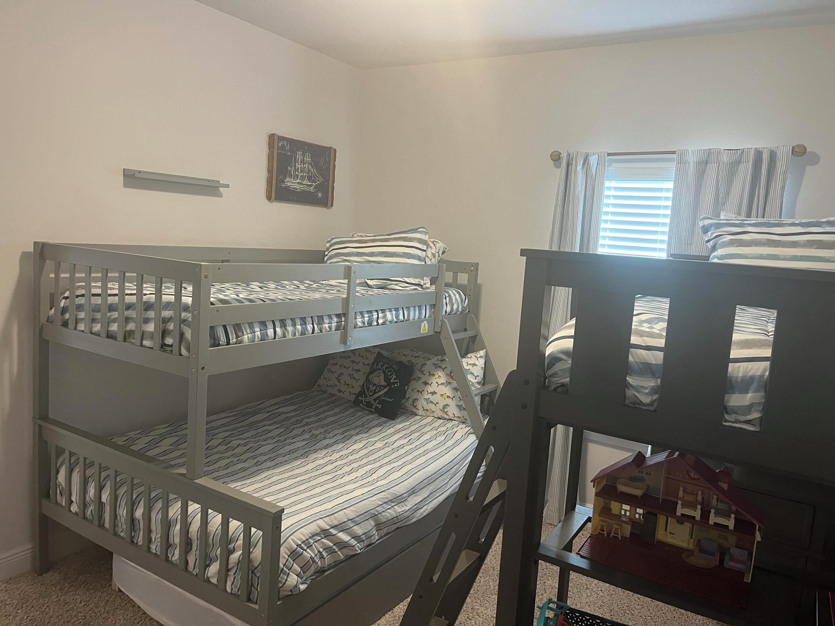 A bunk bed room with striped bedding, a small ship-themed picture, and a dollhouse on a shelf.