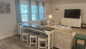 Un salon comprenant un canapé, une table basse, un téléviseur et un coin repas avec des tabourets.