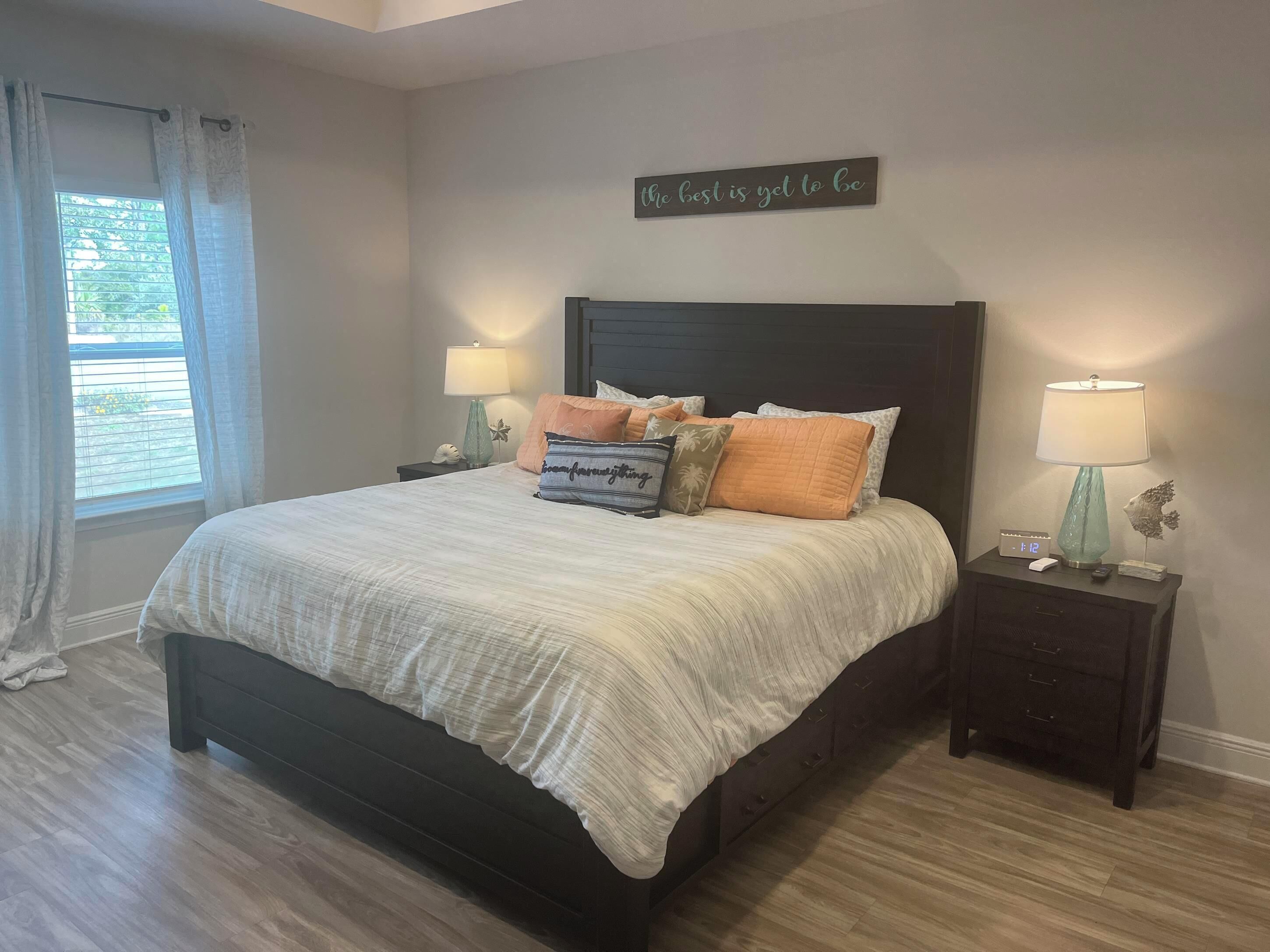 A bedroom with a bed, two bedside tables, a wall clock, and a motivational quote.