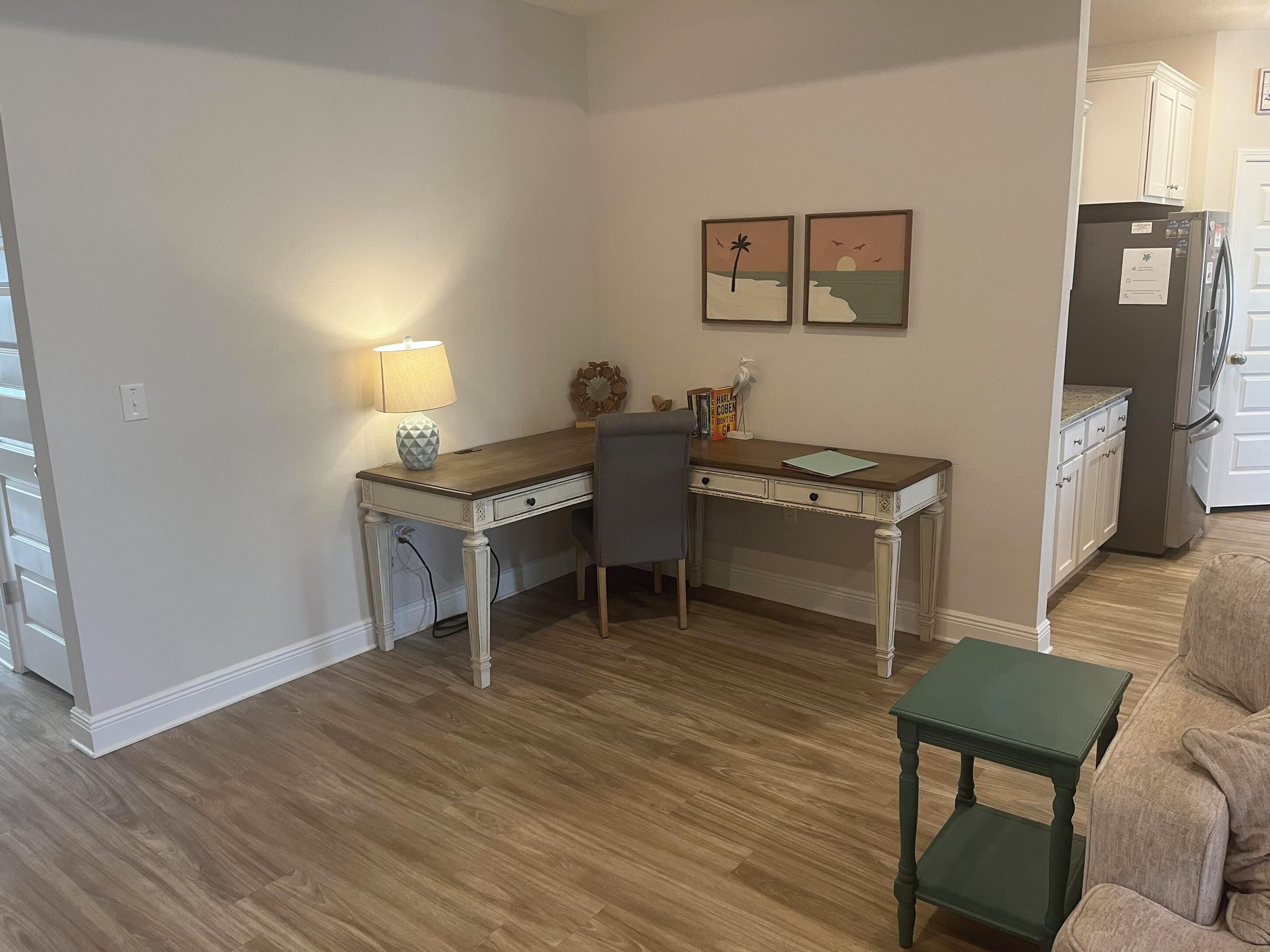 A compact kitchen with a wooden table, a chair, a small green side table, and a refrigerator.