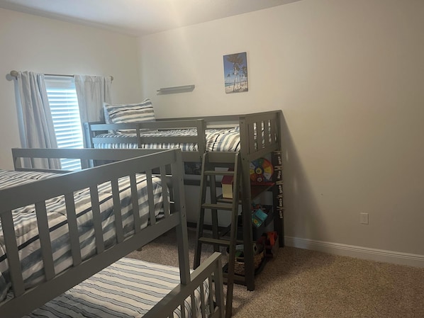 Une chambre avec deux lits superposés, une petite étagère avec des jouets et un tableau sur le thème de la plage accroché au mur.