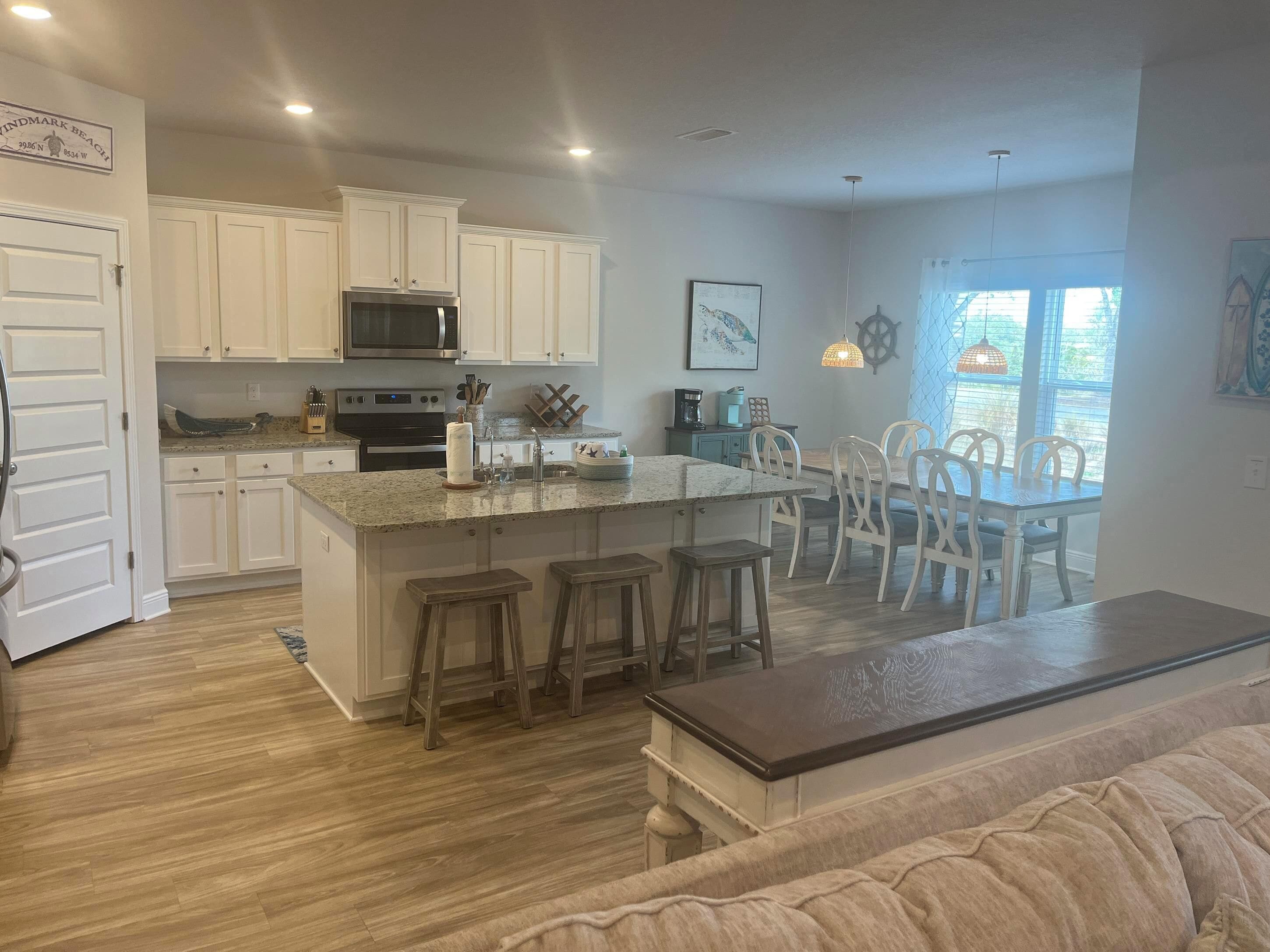 A modern kitchen with white cabinetry, a central island with stools, and a dining area with white chairs.