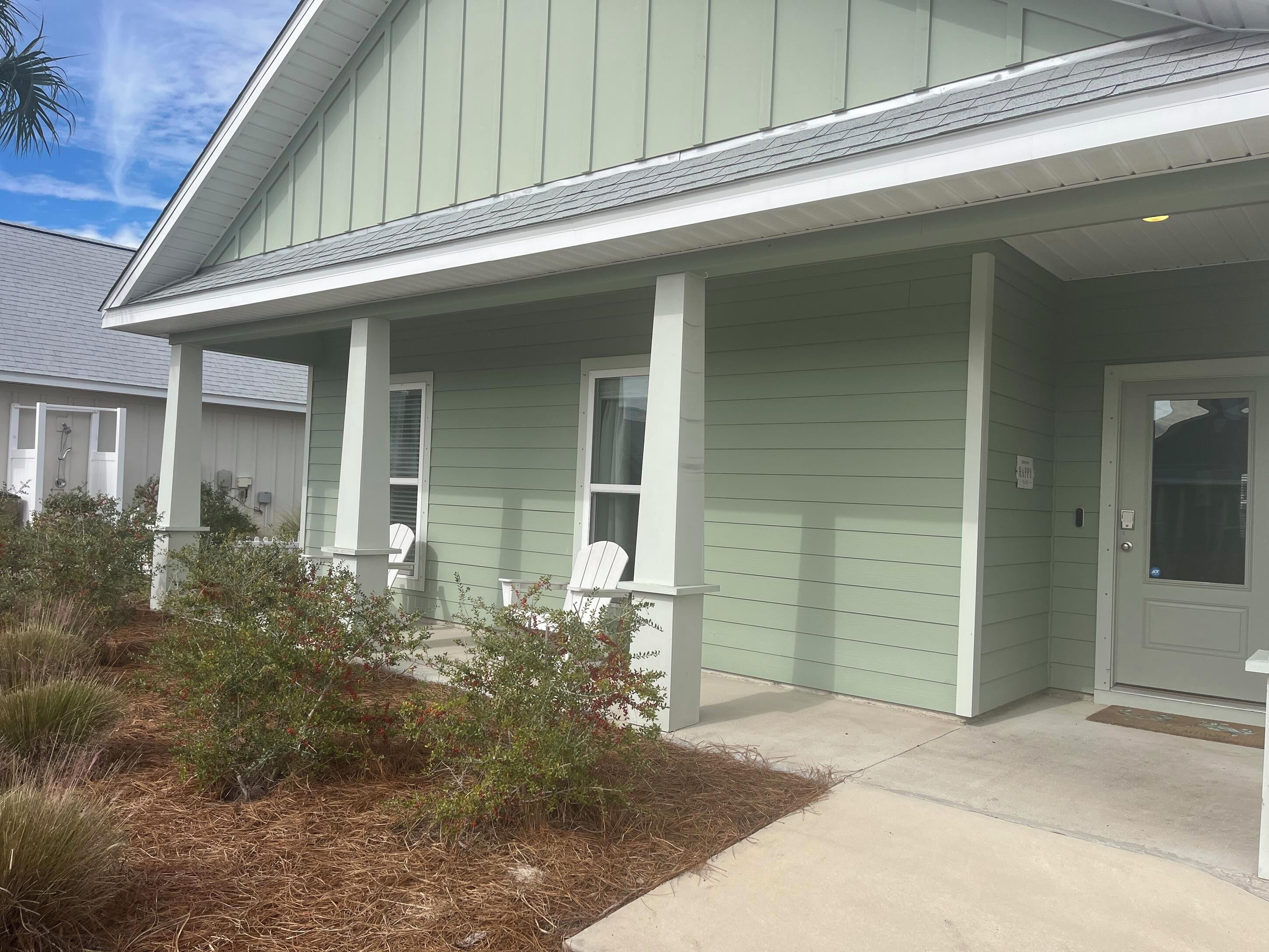 A building with a green exterior, white porch columns, and a door with a window.