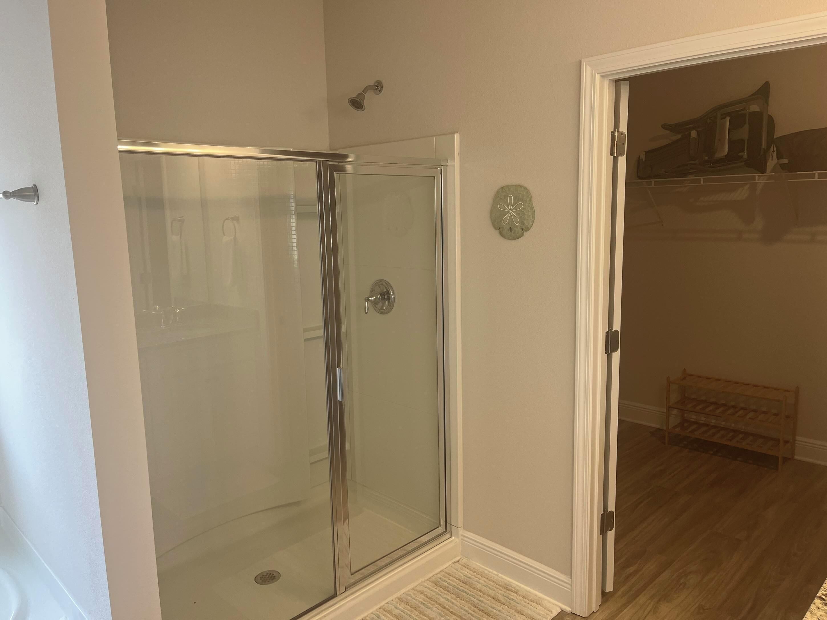 Eine begehbare Dusche mit Glastrennwand und Tür, Holzboden und ein weißer Türrahmen.