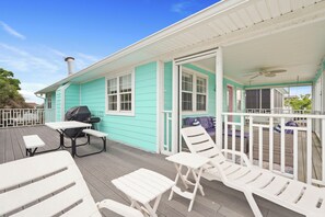 Une maison turquoise avec un porche abrité, des meubles d’extérieur blancs et un barbecue.