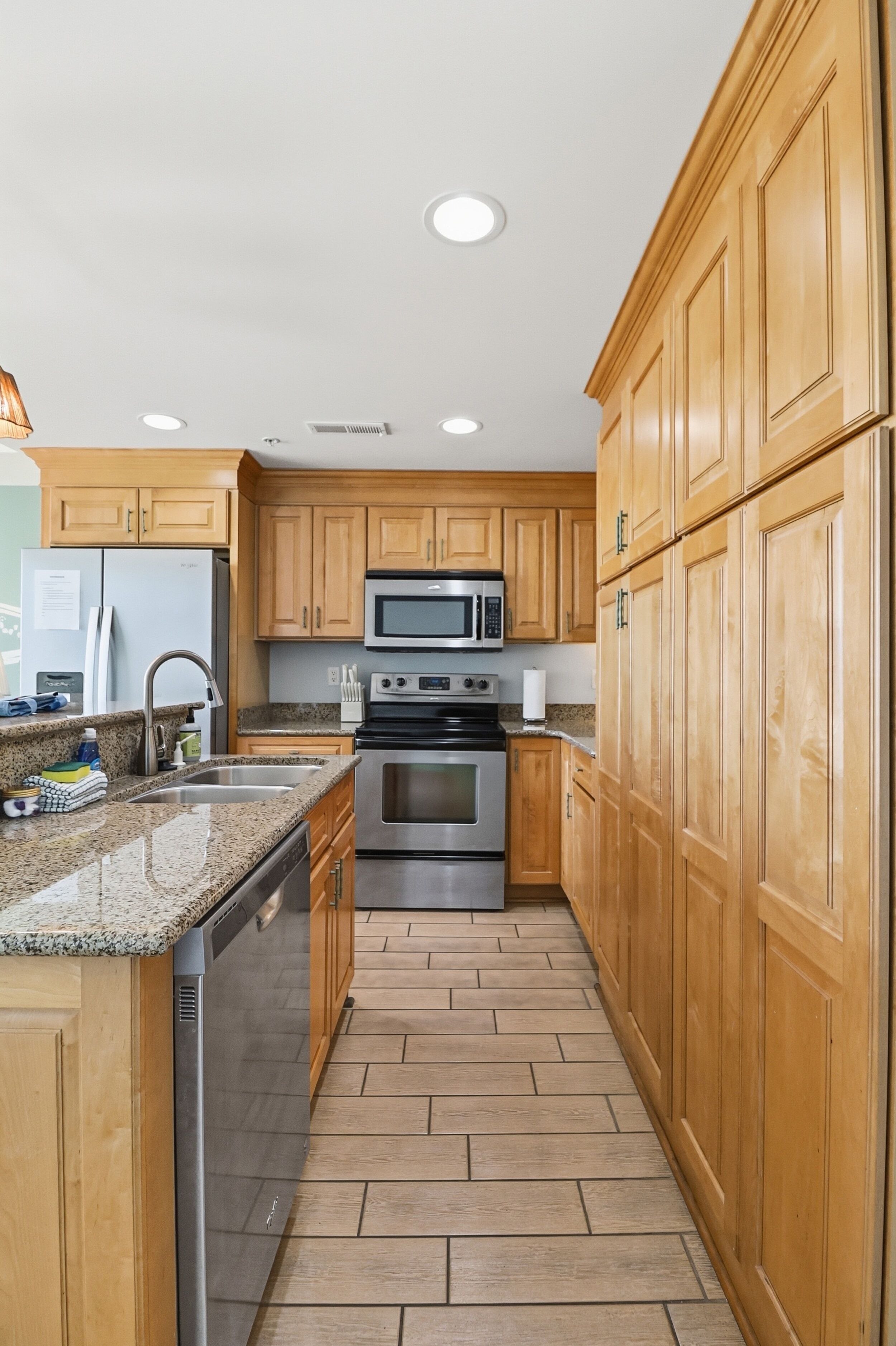 A kitchen with wooden cabinets, stainless steel appliances, and a tiled floor.