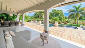 A modern outdoor lounge area with a pool, comfortable seating, and a view of the surrounding greenery. - Villa Bon Bini Verde -Blue Bay Golf & Beach Resort (Sint Michiel)