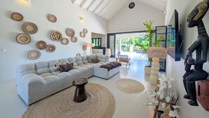 A spacious living room with a large gray sectional sofa, multiple woven wall art pieces, and a modern ceiling design. - Villa Bon Bini Verde -Blue Bay Golf & Beach Resort (Sint Michiel)