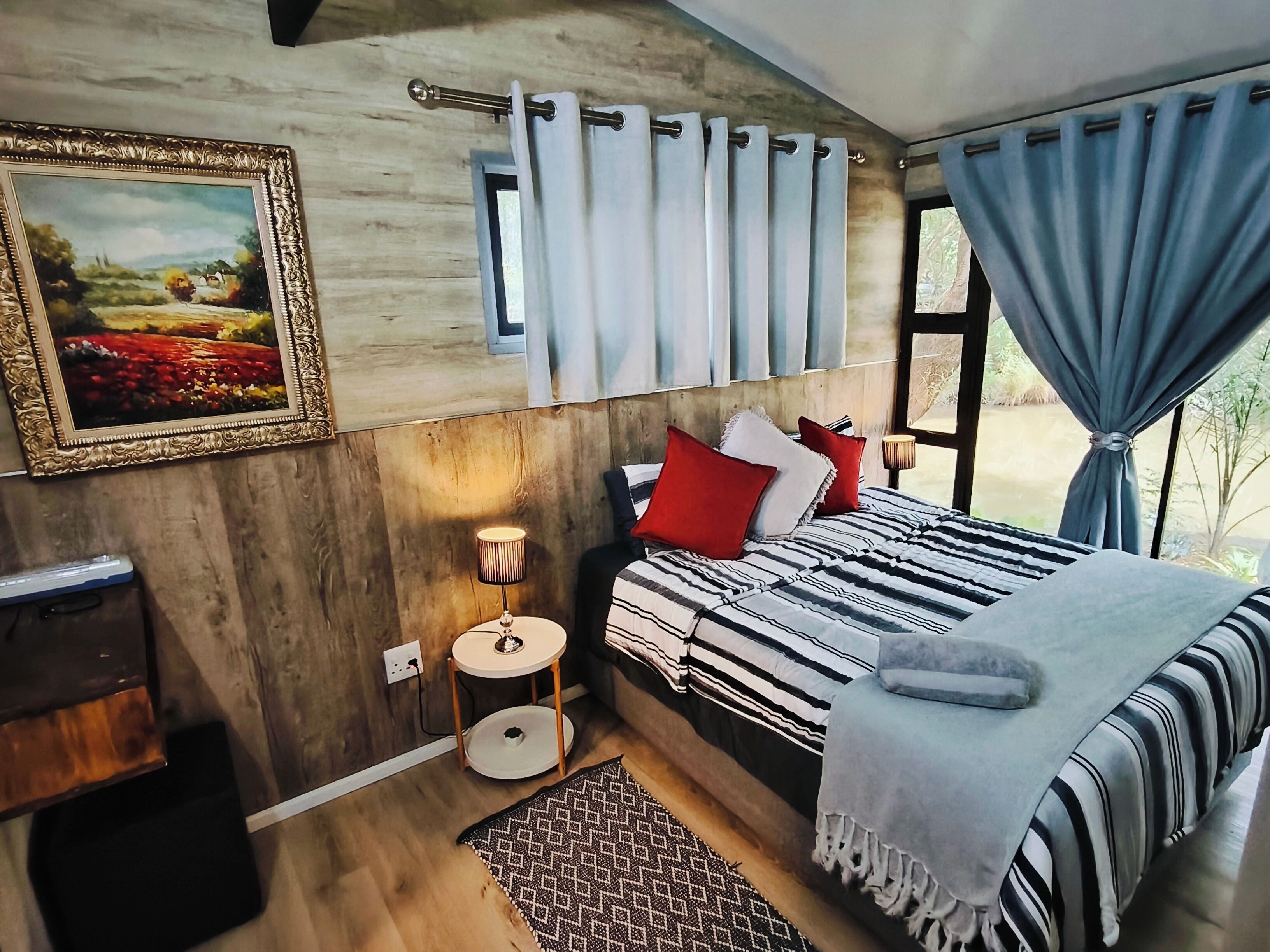 Un dormitorio con cama, mesita de noche, lámpara, un cuadro enmarcado y cortinas.