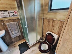 Un baño con piso de madera, un inodoro, una ducha con puerta de vidrio y un letrero que indica 'LUSH ONLY' papel higiénico y eliminación de residuos naturales.
