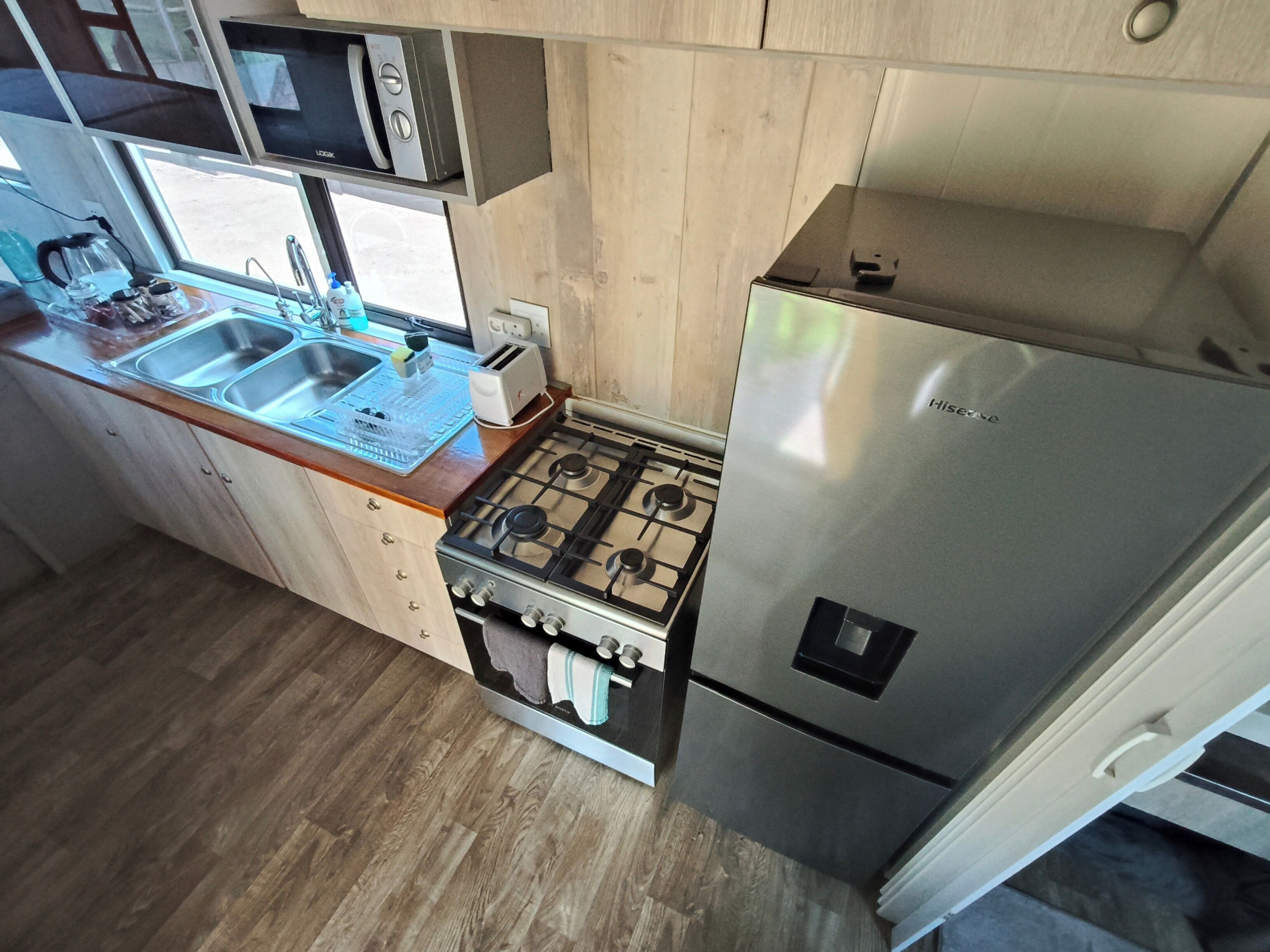 A compact kitchen with a gas stove, a stainless steel refrigerator, a microwave, and a sink with a dish rack.