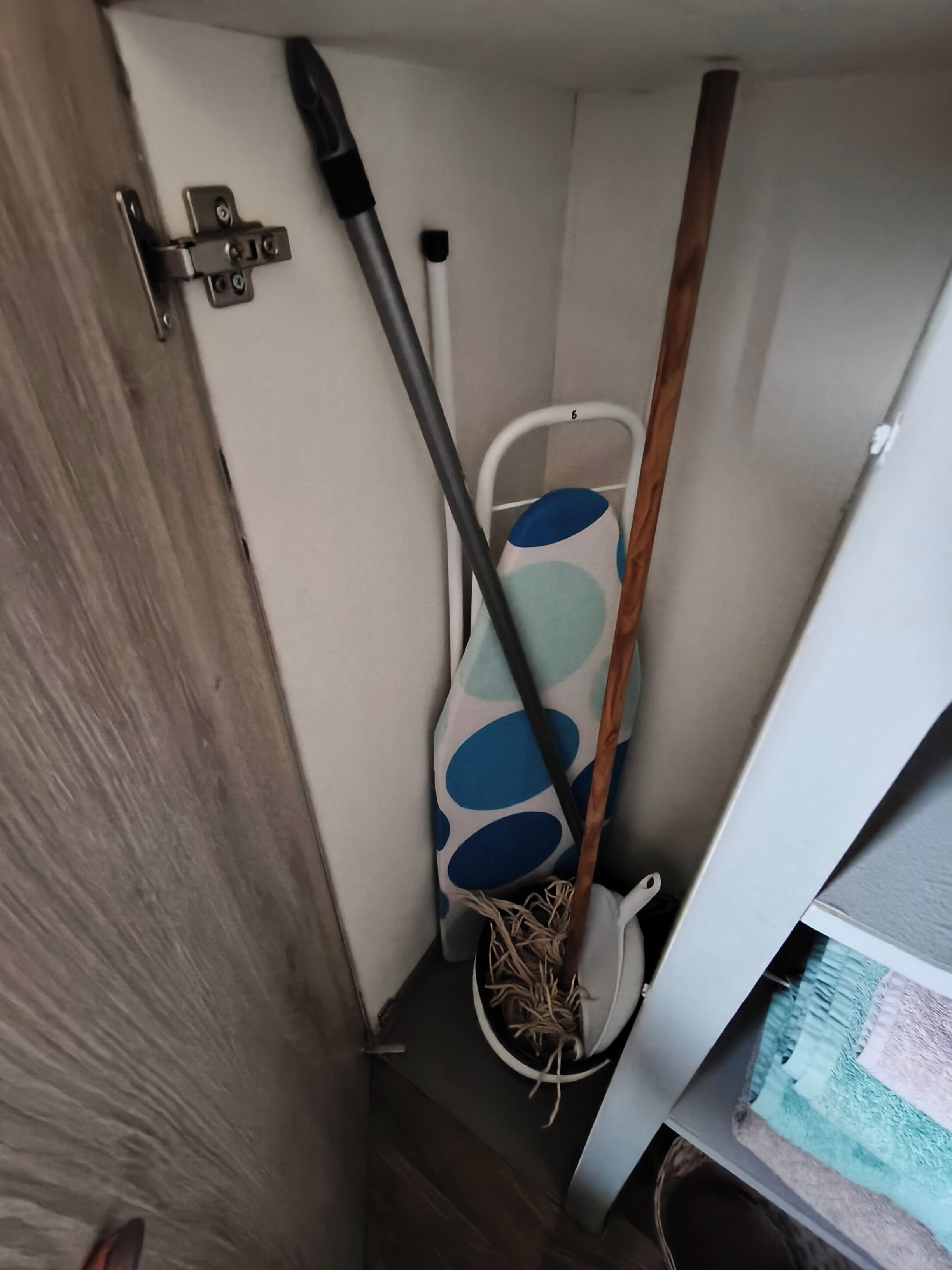 Una esquina de una habitación con piso de madera, pared blanca y una puerta con un cierre metálico.