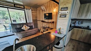 A modern kitchen with a granite countertop, stainless steel sink, and wooden cabinets. There is a television mounted on the wall and a sign with motivational quotes. - Lost Valley Farm Lodge (Rustenburg)