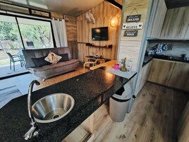Una cocina moderna con encimera de granito, pileta de acero inoxidable y armarios de madera. Hay un televisor montado en la pared y un cartel con citas motivacionales.