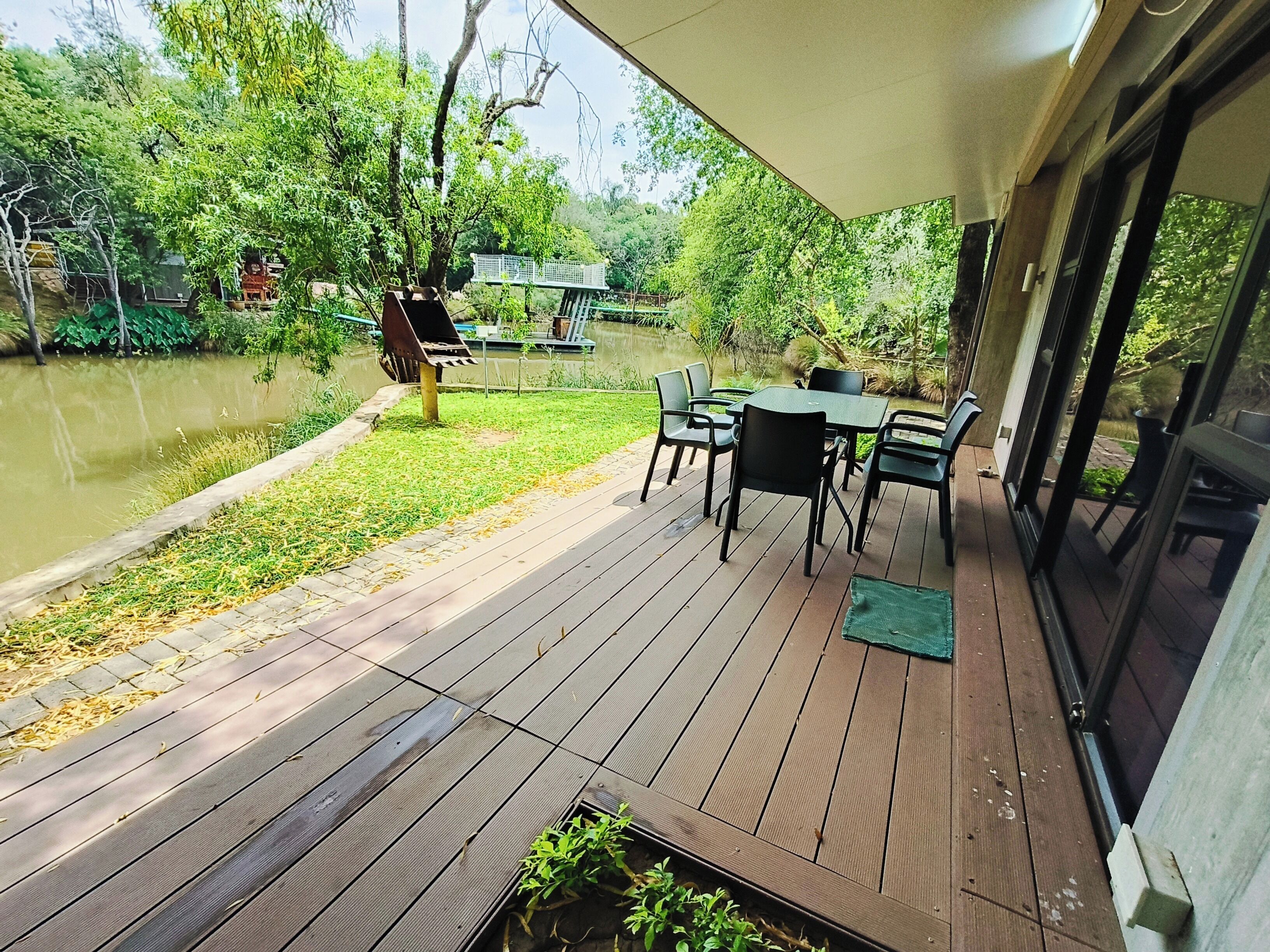 A wooden deck with a table and chairs, overlooking a body of water and greenery.