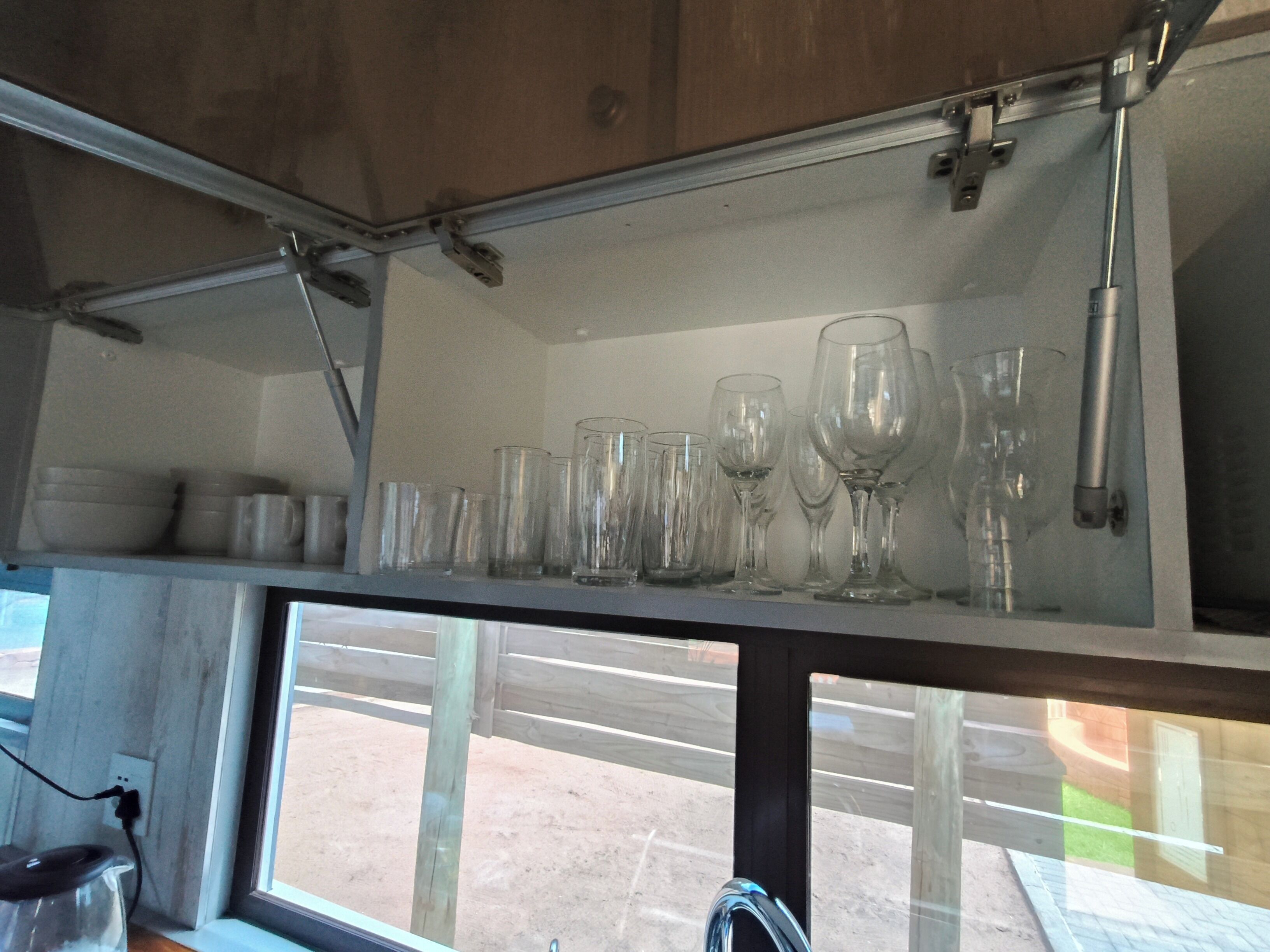 Una cucina con una dispensa che contiene diversi bicchieri e un bollitore sul piano di lavoro.