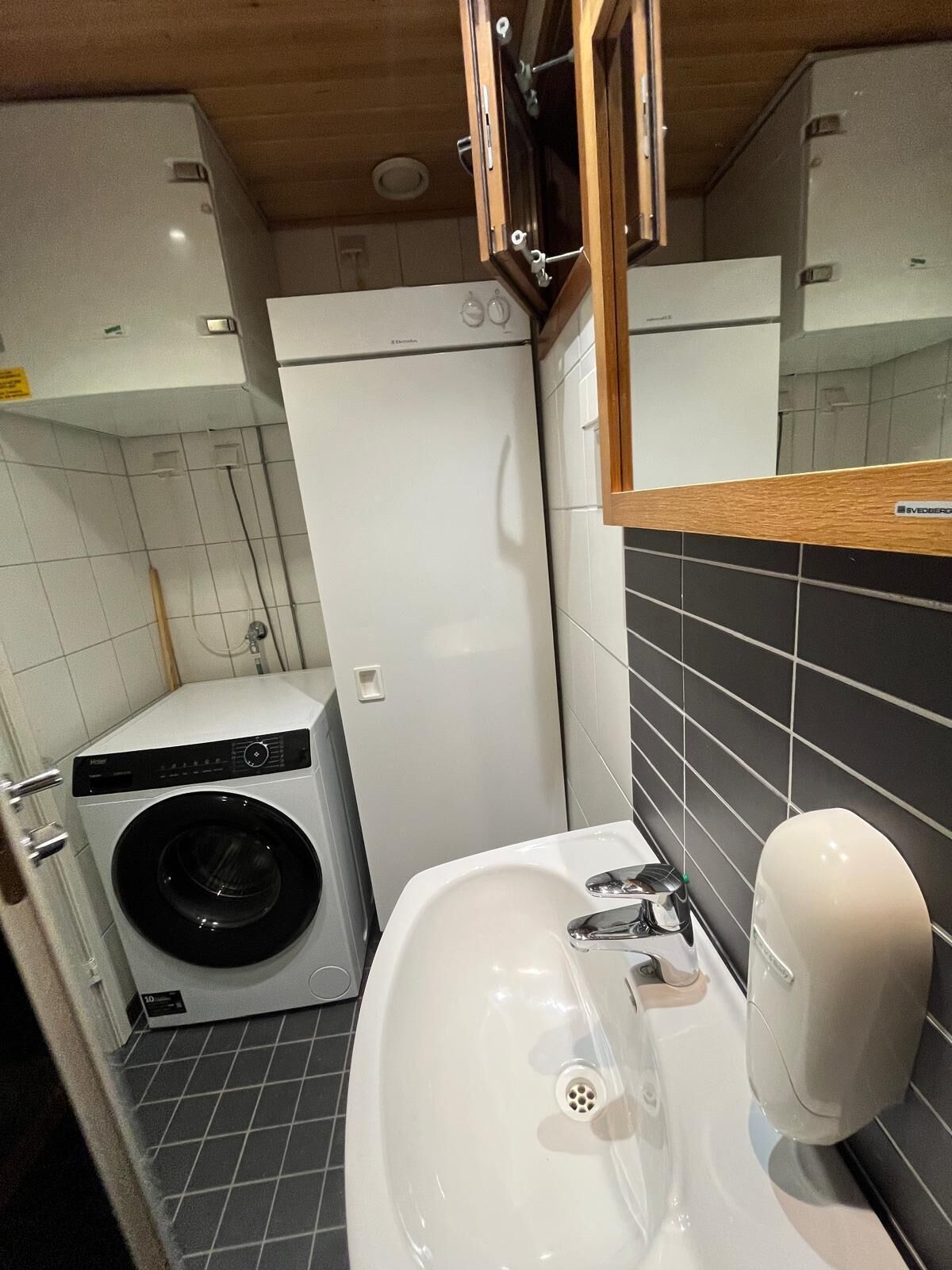 Une petite salle de bain équipée d’un lave-linge, d’un lavabo avec un distributeur de savon et d’un miroir.