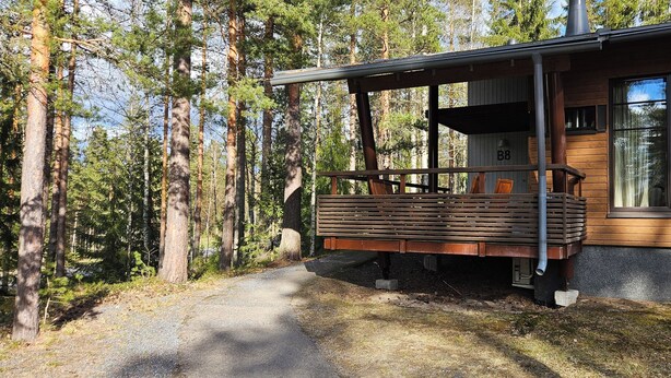 A cabin with a wooden deck, a covered porch, and a large window.