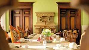 Une salle à manger élégante, avec une grande table dressée pour un repas, entourée de chaises en bois et agrémentée d’une cheminée décorative.