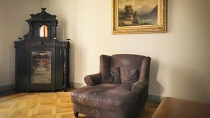 Une pièce comprenant un fauteuil en cuir marron, un buffet en bois foncé orné de motifs complexes et un tableau représentant un paysage, accroché au mur.