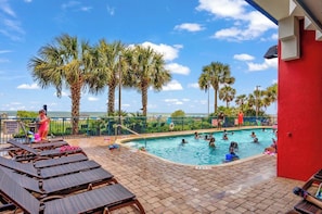 A pool area with lounge chairs, palm trees, and a view of the ocean. - Ocean Front Luxury! 3BR Resort Amenities, 20th Floor condo (Myrtle Beach)