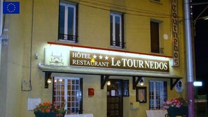 Un hotel anomenat "Le Tournedos" amb un cartell, seients a l'exterior i testos de flors.