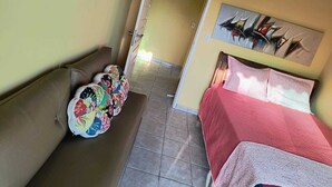 Een smalle gang met een bed aan de rechterkant, een deur aan het einde en een kleurrijke quilt aan de linkerkant.
