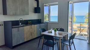 A modern kitchen with a large window, a dining area with a table and chairs, and a view of the ocean. - Fronte mare Levante - primo piano (Montegiordano, Cosenza)
