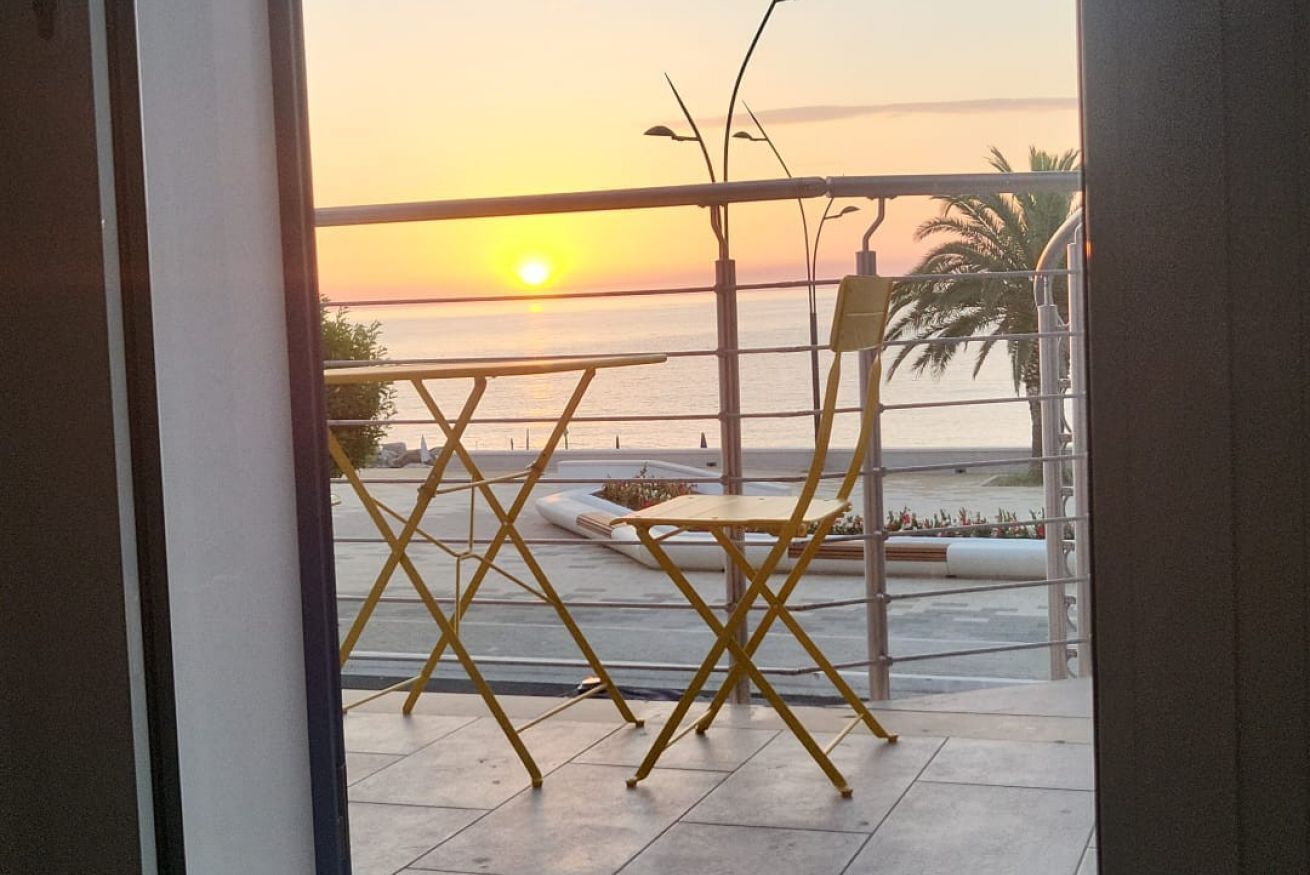A balcony with a view of the sunset over the sea, a folding chair, and a small table.