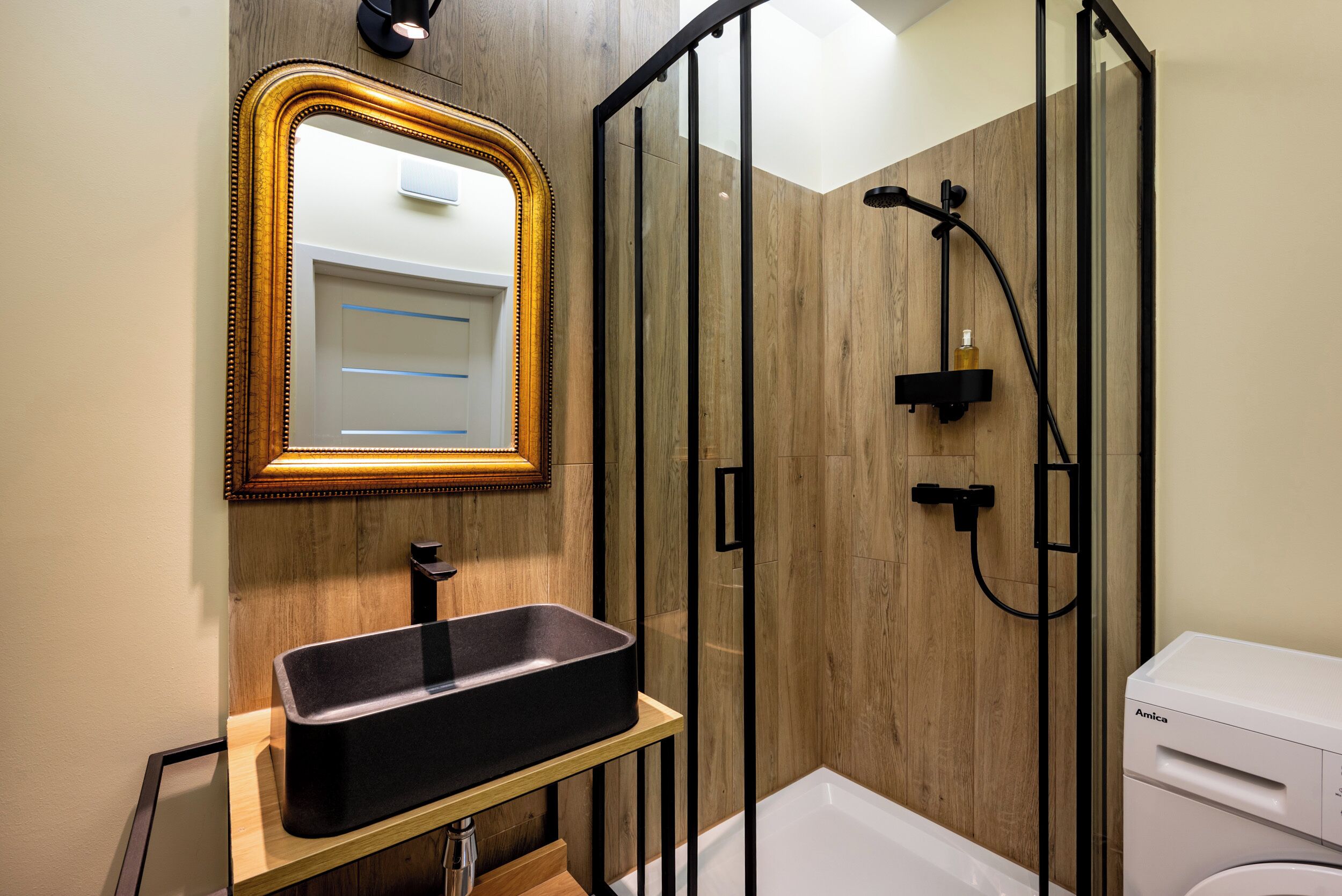 Une salle de bain moderne avec un meuble-lavabo en bois, un évier noir, une douche en verre et des toilettes blanches.