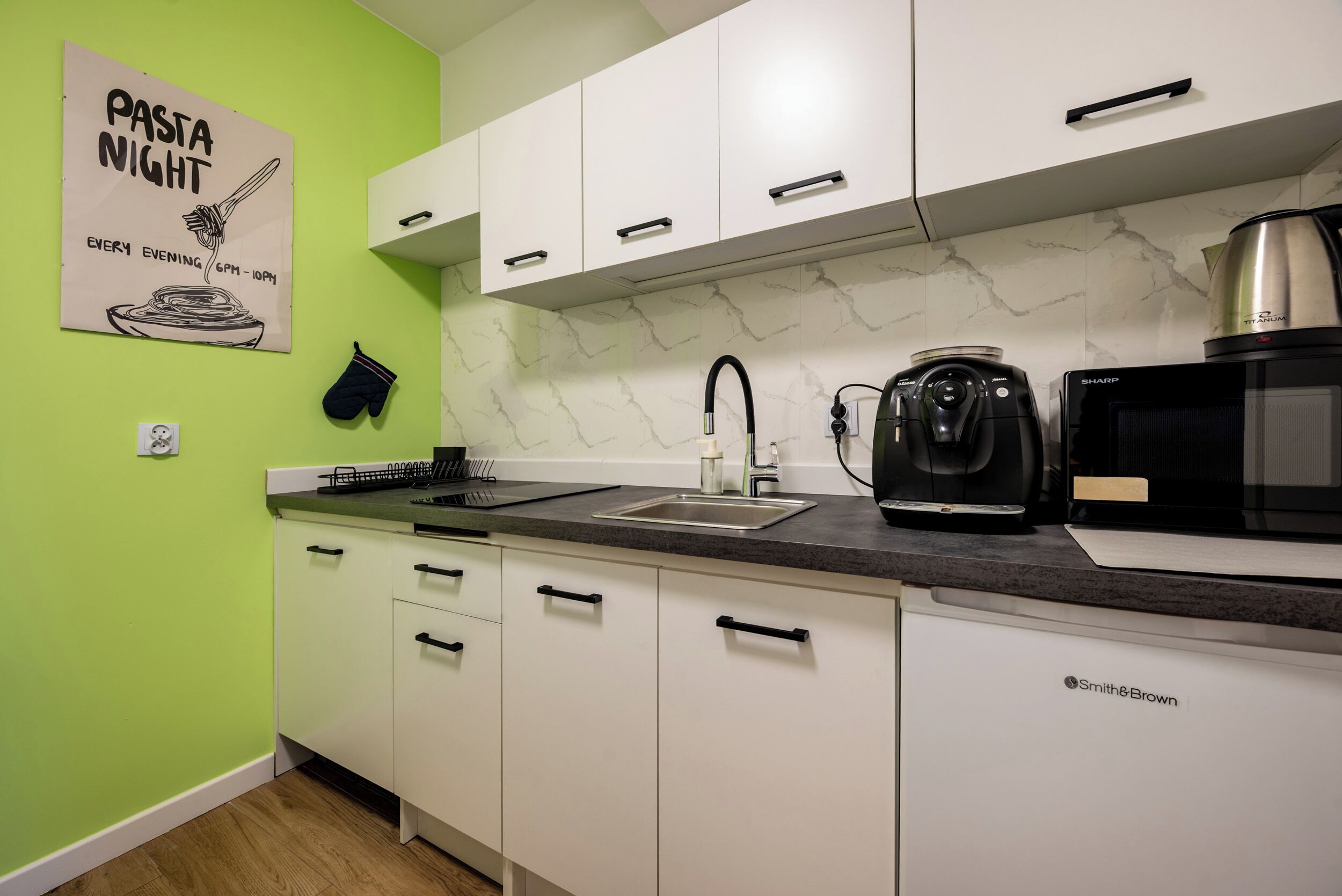 A kitchen with white cabinets, a black countertop, a sink, a coffee maker, and a microwave.