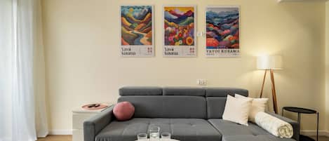 A modern living room with a grey sofa, a white coffee table, and three framed artworks on the wall.