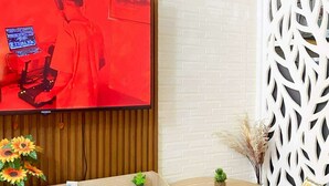 Un soggiorno moderno con televisione a schermo piatto montata su una parete in legno, un tavolino rotondo con due sedie, un pannello decorativo bianco e una piccola pianta in vaso.