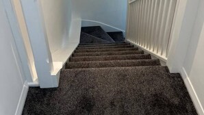 Una escalera con peldaños alfombrados y barandillas blancas.