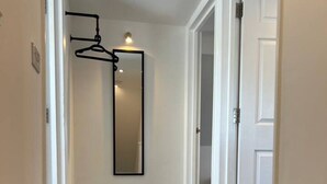 Un pasillo con alfombra gris, paredes blancas y un perchero negro con espejo.