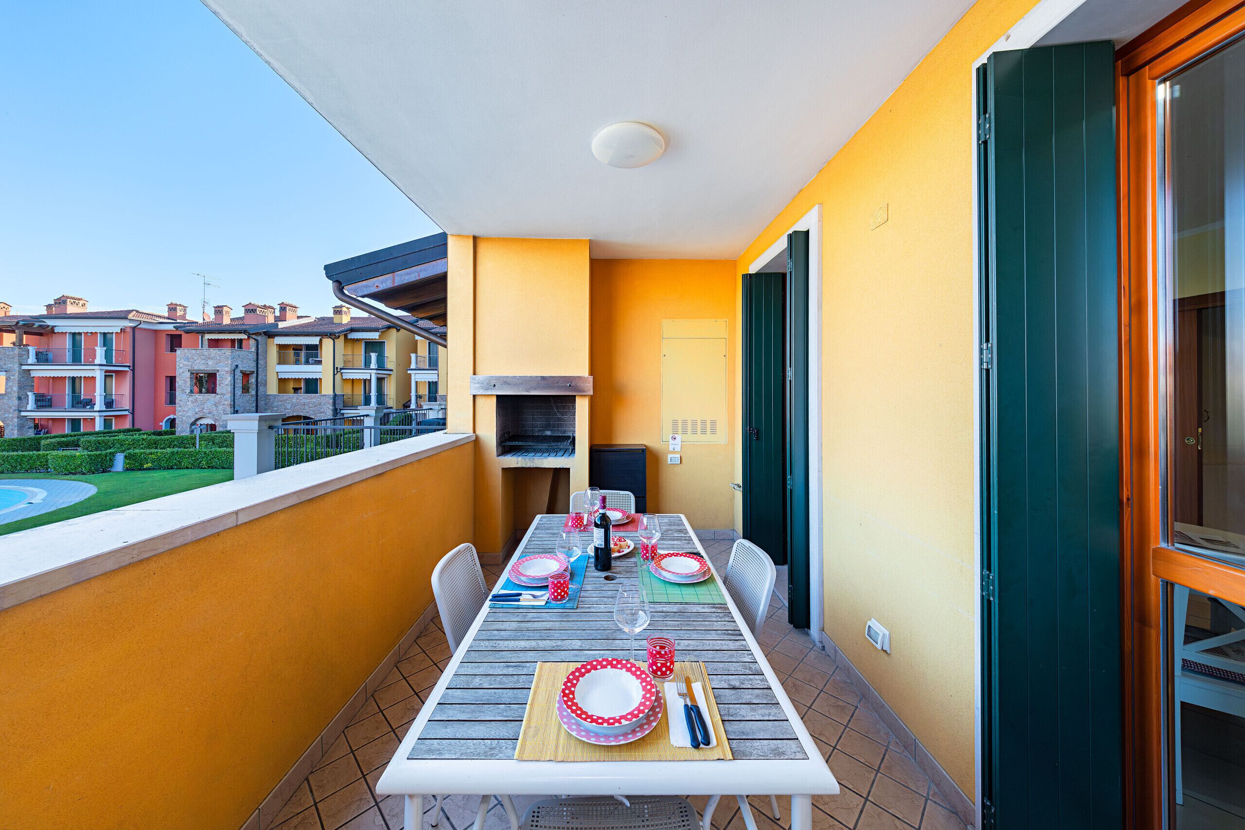 Un balcon avec une table à manger pour quatre personnes, un barbecue et une vue sur les immeubles voisins.