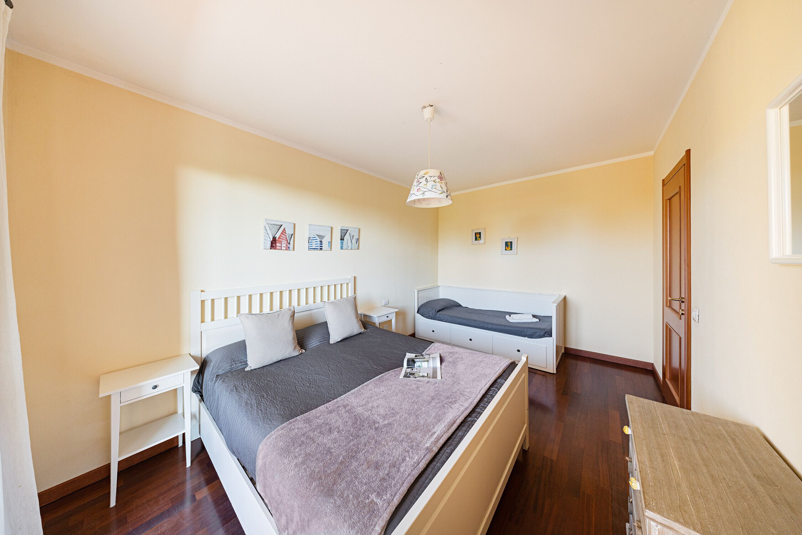 A bedroom with a bed, bedside tables, a nightstand, a dresser, and a hanging light fixture.