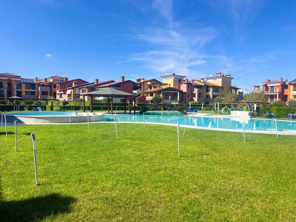 Area piscina con gazebo, circondata da prato curato e palazzi a più piani con balconi.