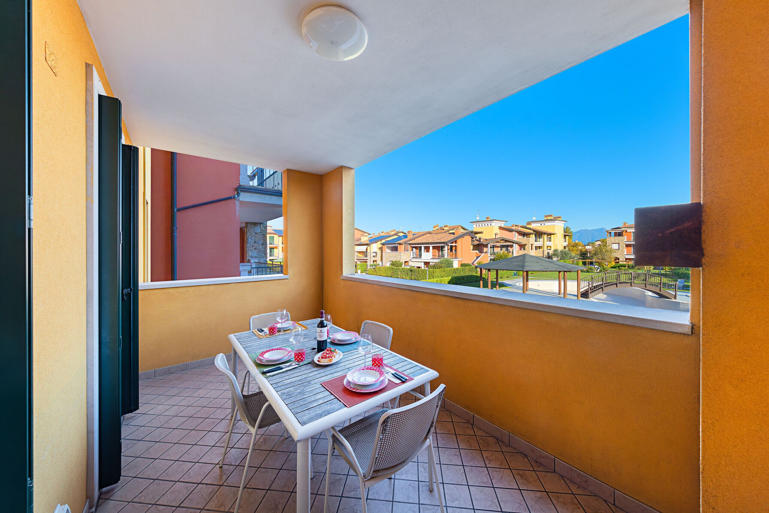 A balcony with a table set for dining, a chair, and a view of buildings in the distance.