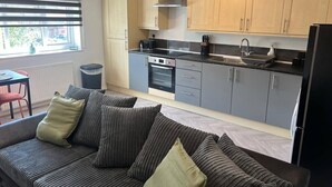 A compact kitchen with grey cabinets, a black refrigerator, and a dining area with a red chair. - Gatwick 2 bedroom Apartment (Grasmere)