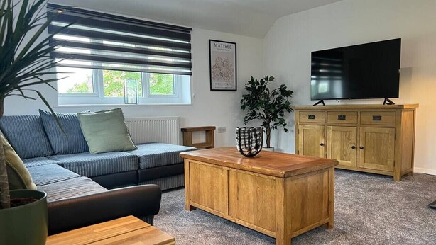 A living room with a sofa, coffee table, TV, and wooden cabinet. - Gatwick 2 bedroom Apartment (Grasmere)