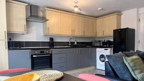 A compact kitchen with modern appliances, a dining area with a table and chairs, and a washing machine in the background. - Gatwick 2 bedroom Apartment (Grasmere)