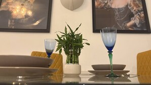 A dining table with a vase of green plants, two blue glassware, and a framed portrait above. - Spacious 2 bed apartment in Addlestone (Surrey)
