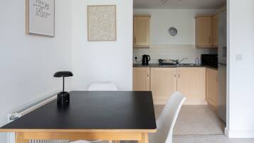 A modern kitchen with light wooden cabinets, a black countertop, and a wall-mounted clock.