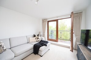 Ein modernes Wohnzimmer mit einem grauen Sofa, einer schwarzen Decke und einem Fernseher auf einem Holzständer.
