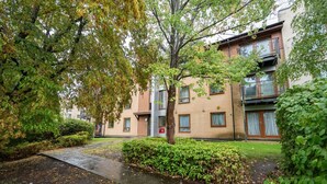 A multi-story residential building with a brick facade, a visible entrance, and a small garden area with a pathway. - 2 Bedroom Flat Free Parking Close to Gatwick (West Sussex)